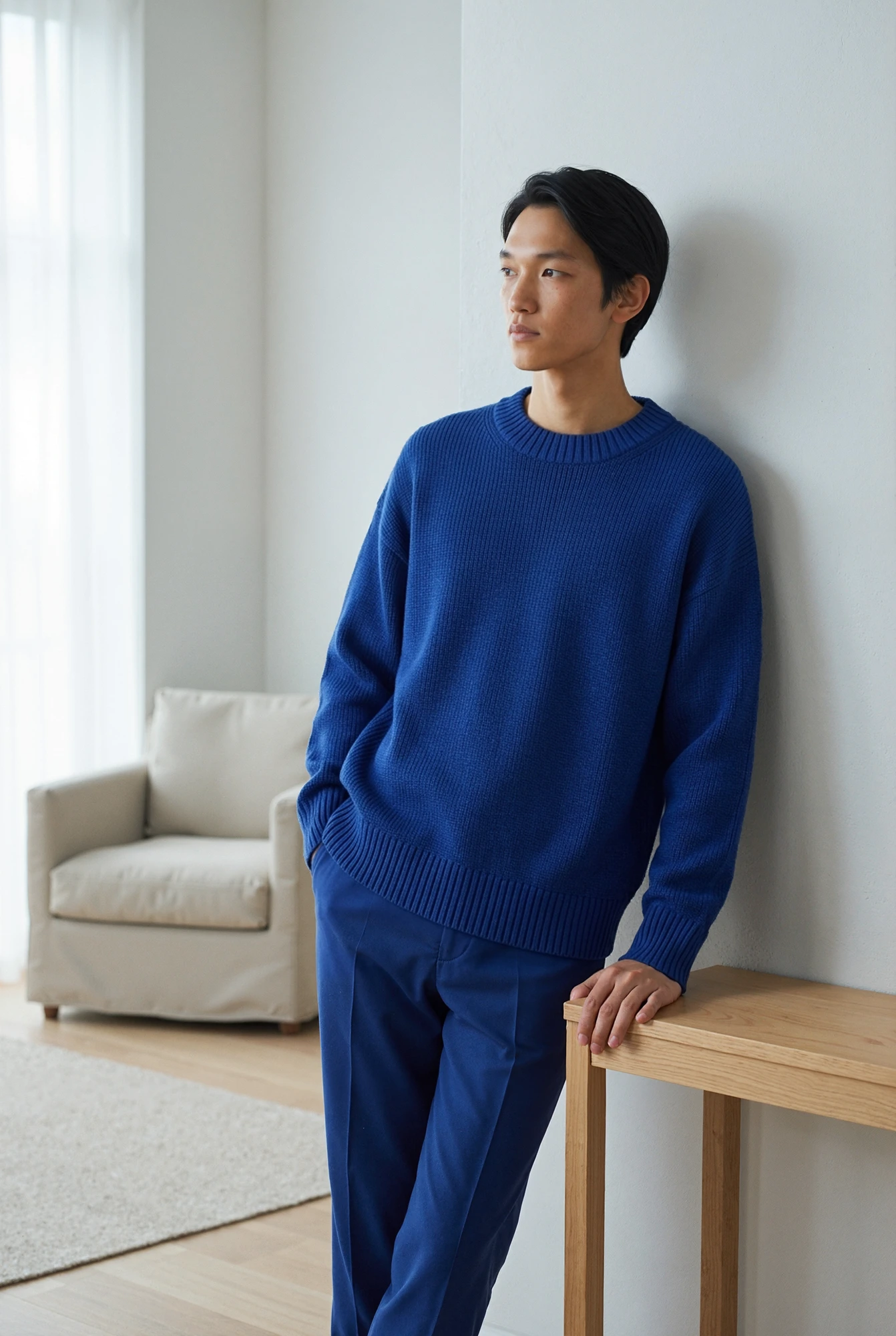 Male model in a blue knit sweater leaning against a wall.